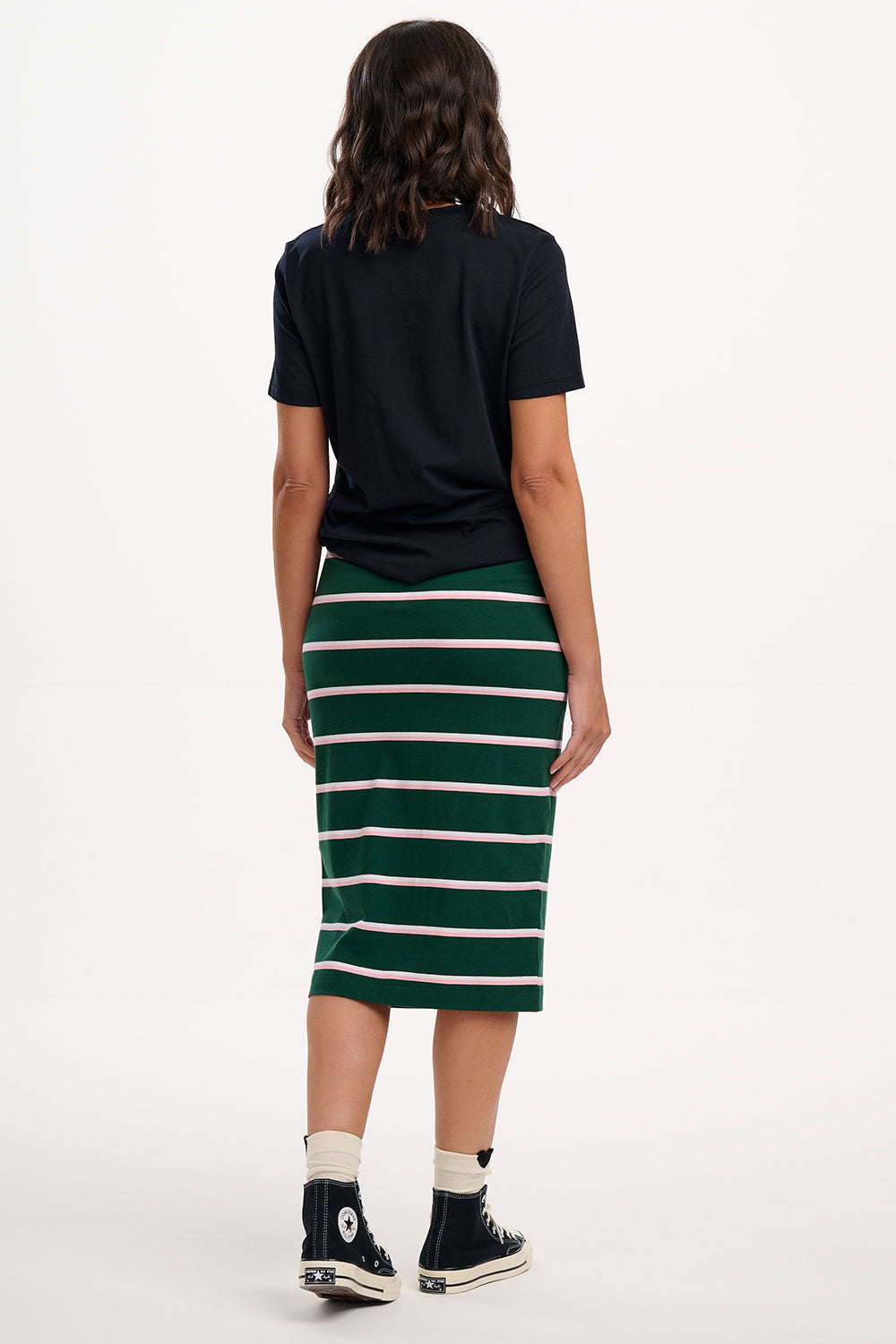 Sugarhill Brighton model wearing a black t-shirt and green striped skirt on a white background