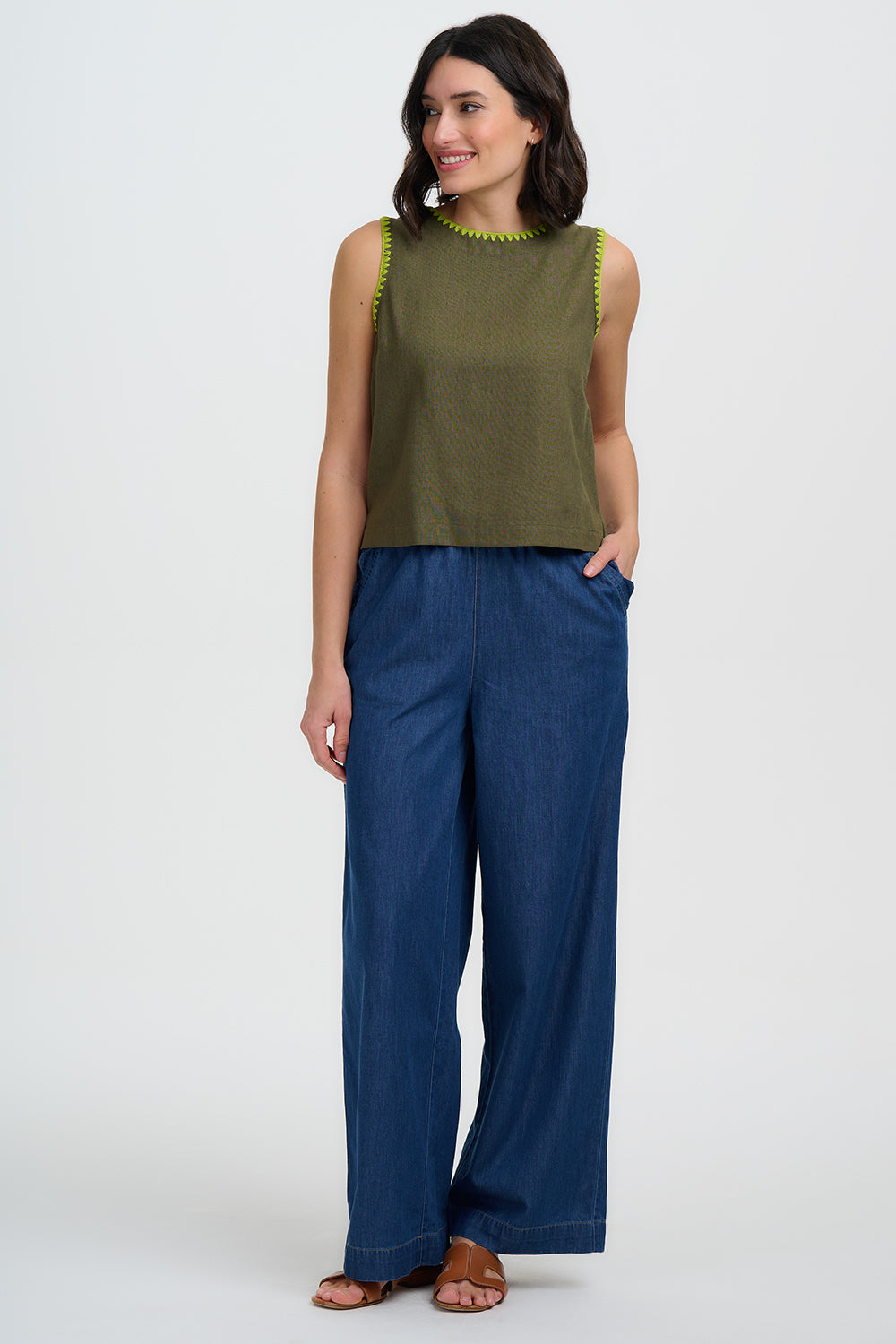 Woman wearing a green sleeveless top and blue pants on a white background