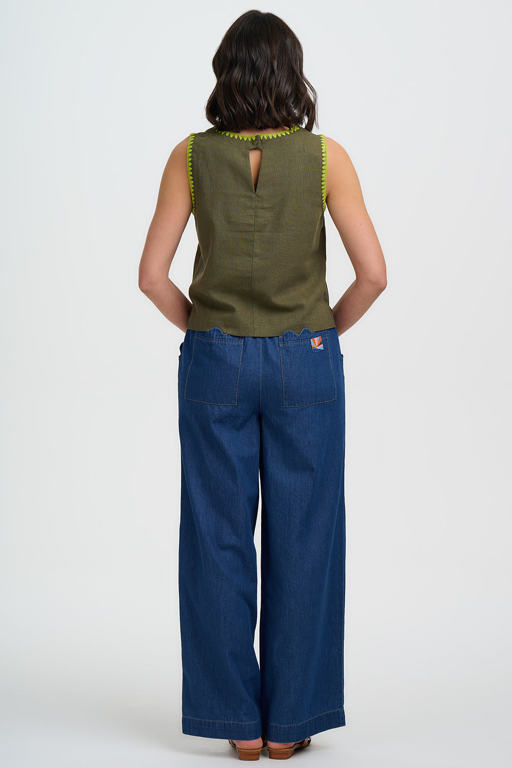Woman wearing a green sleeveless top and blue pants on a white background