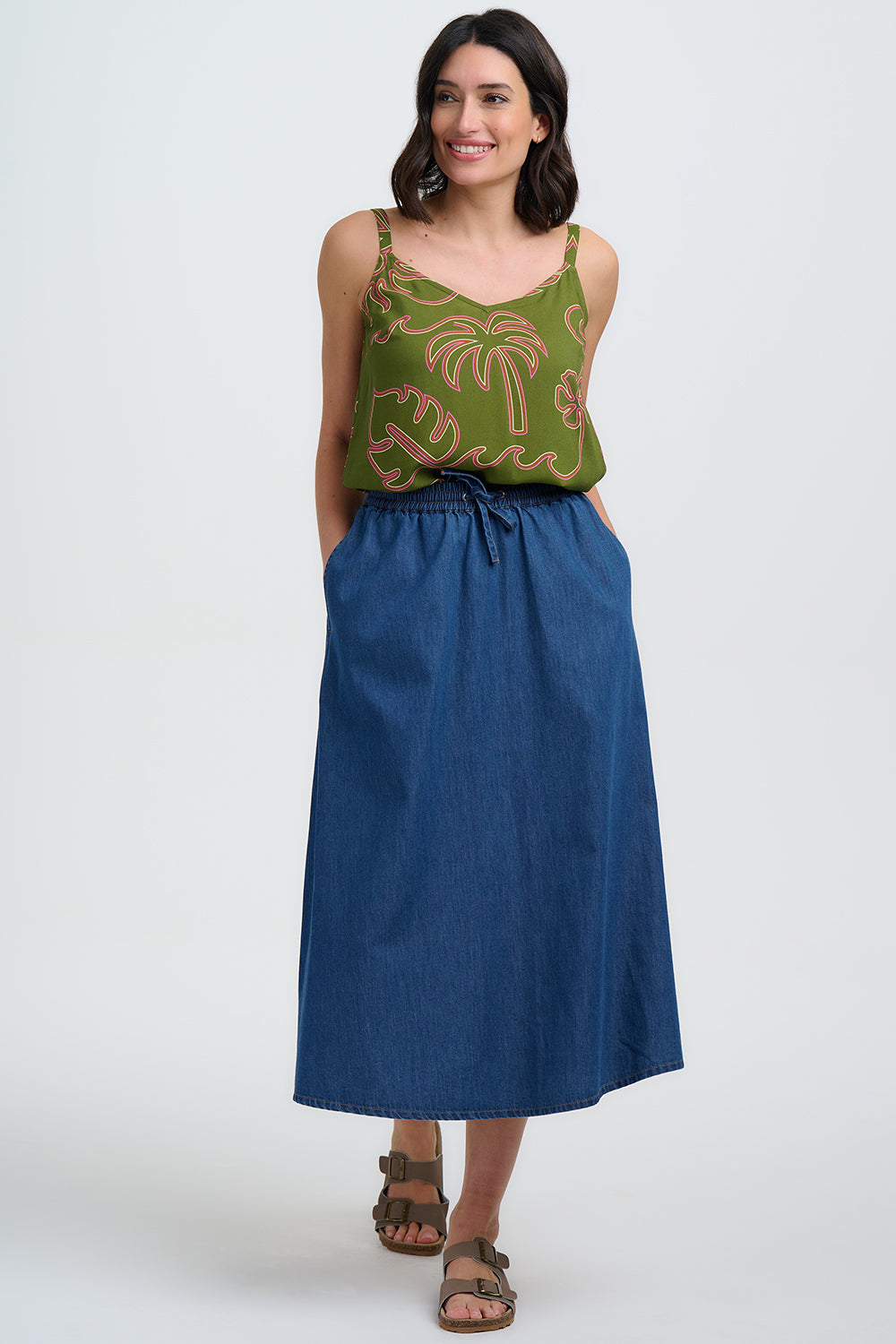 Woman wearing a green patterned top and blue skirt on a white background