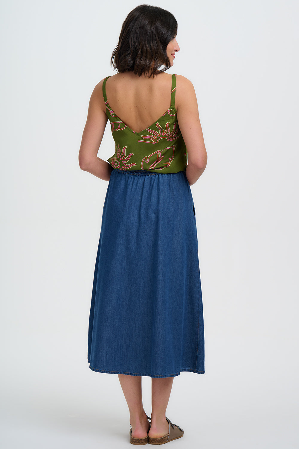 Woman wearing a green patterned top and blue skirt on a white background