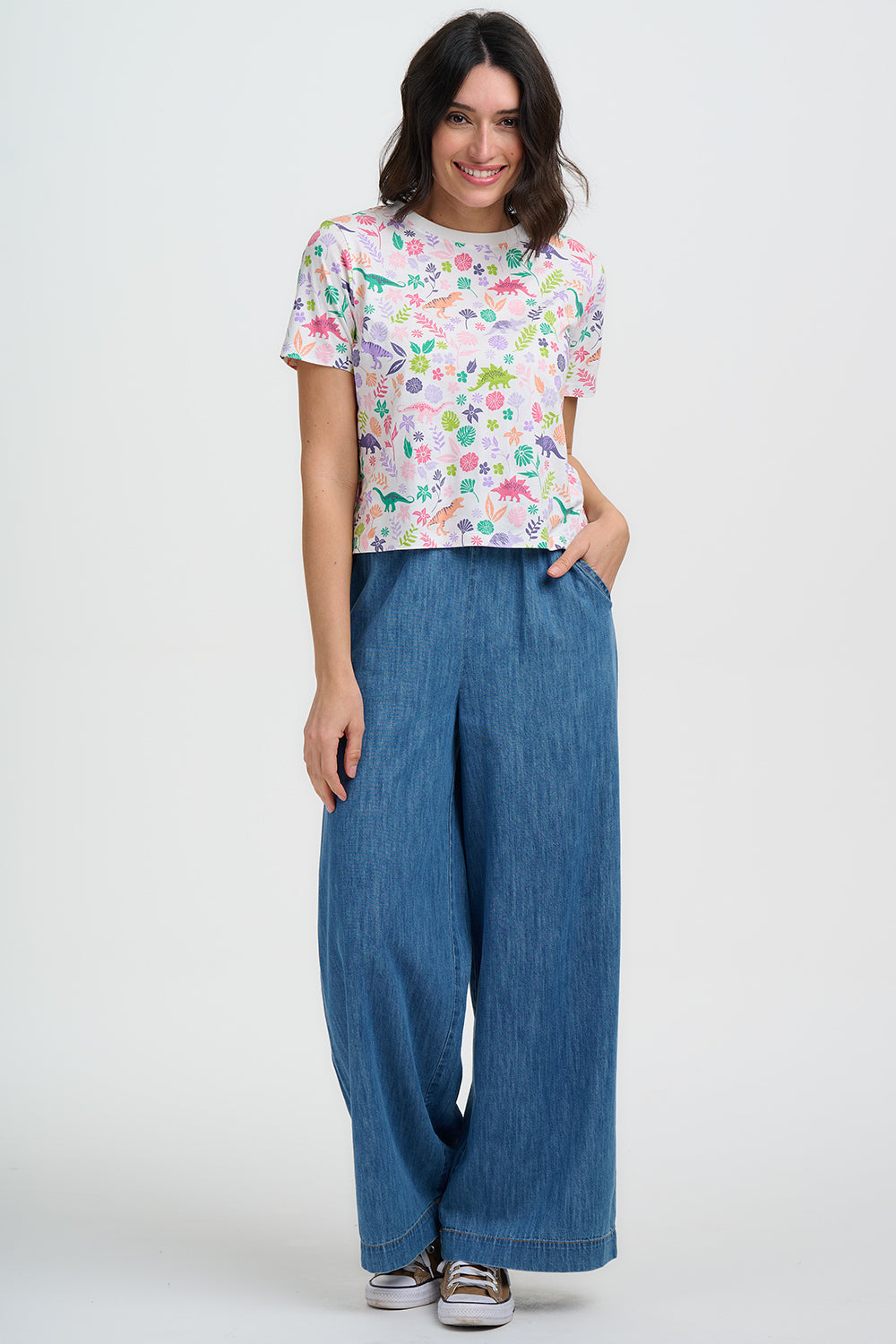 Woman wearing a colorful patterned shirt and blue wide-leg pants on a white background