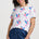 Woman wearing a white t-shirt with colorful parrot patterns and blue pants on a plain background