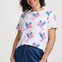 Woman wearing a white t-shirt with colorful parrot patterns and blue pants on a plain background