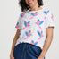 Woman wearing a white t-shirt with colorful parrot patterns and blue pants on a plain background
