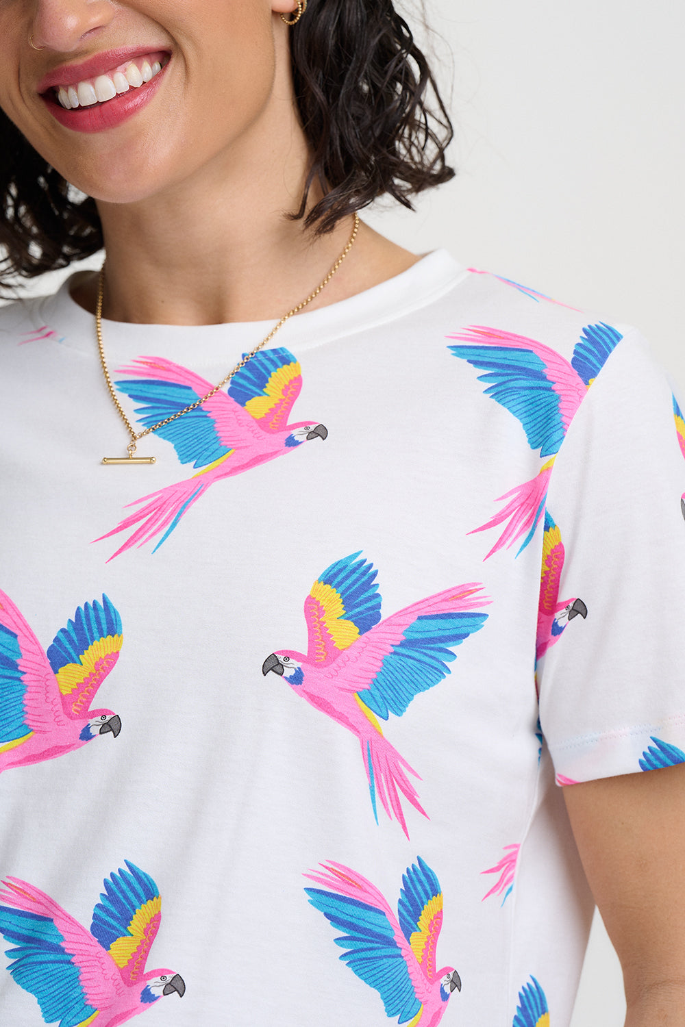 Person wearing a white t-shirt with colorful parrot patterns on a plain background