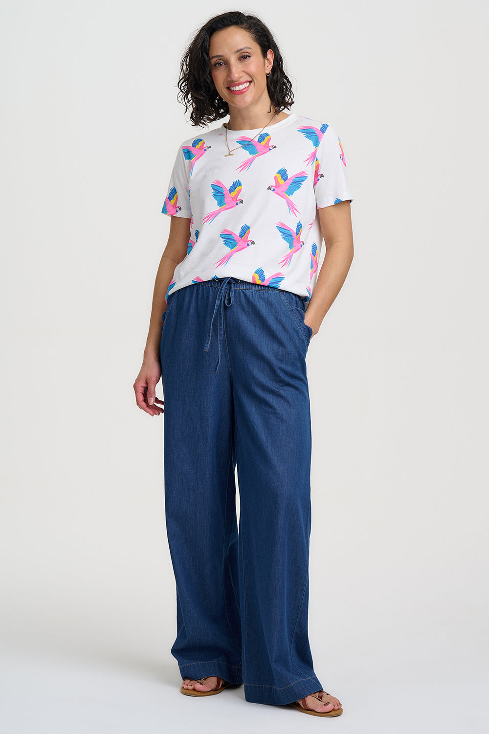 Woman wearing a colorful parrot-patterned shirt and blue pants on a white background