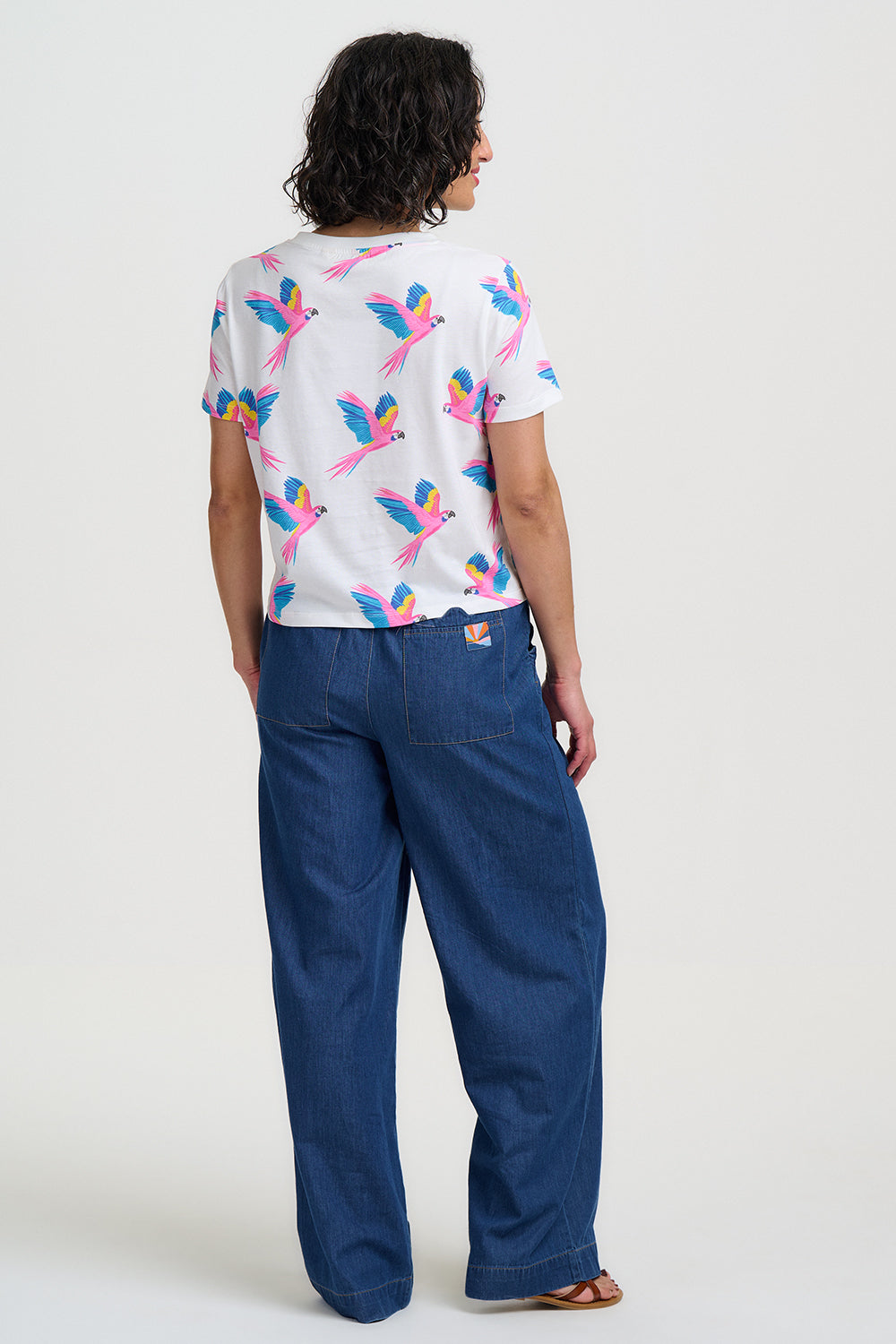 Person wearing a white t-shirt with colorful parrot design and blue pants on a white background