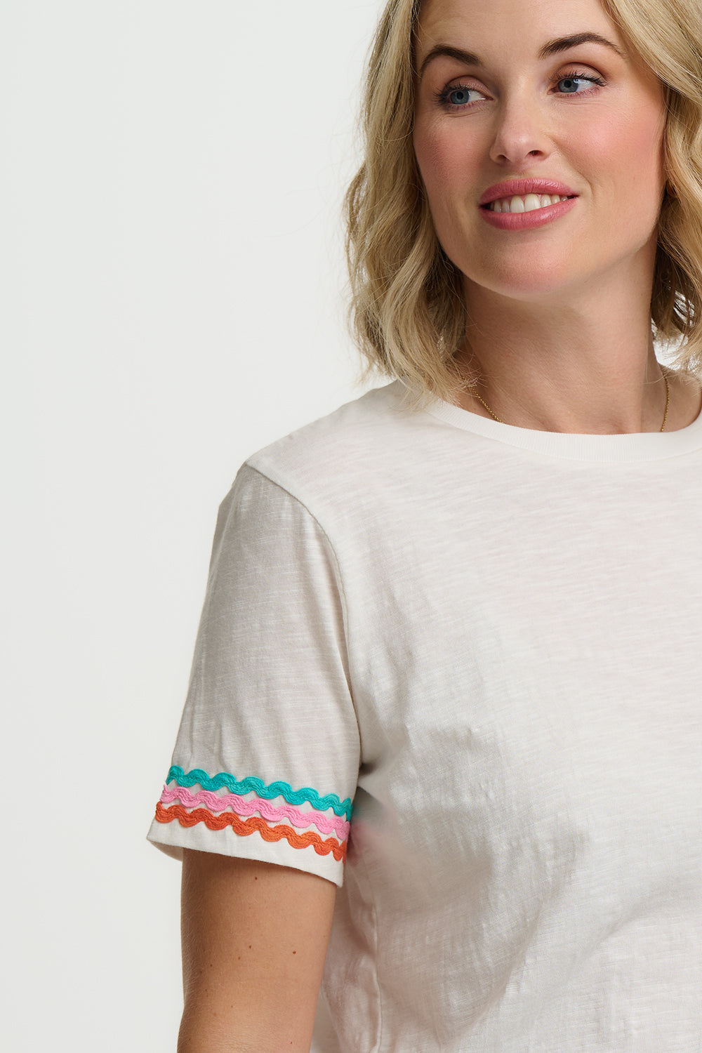 Woman wearing a white top with colorful sleeves on a plain background