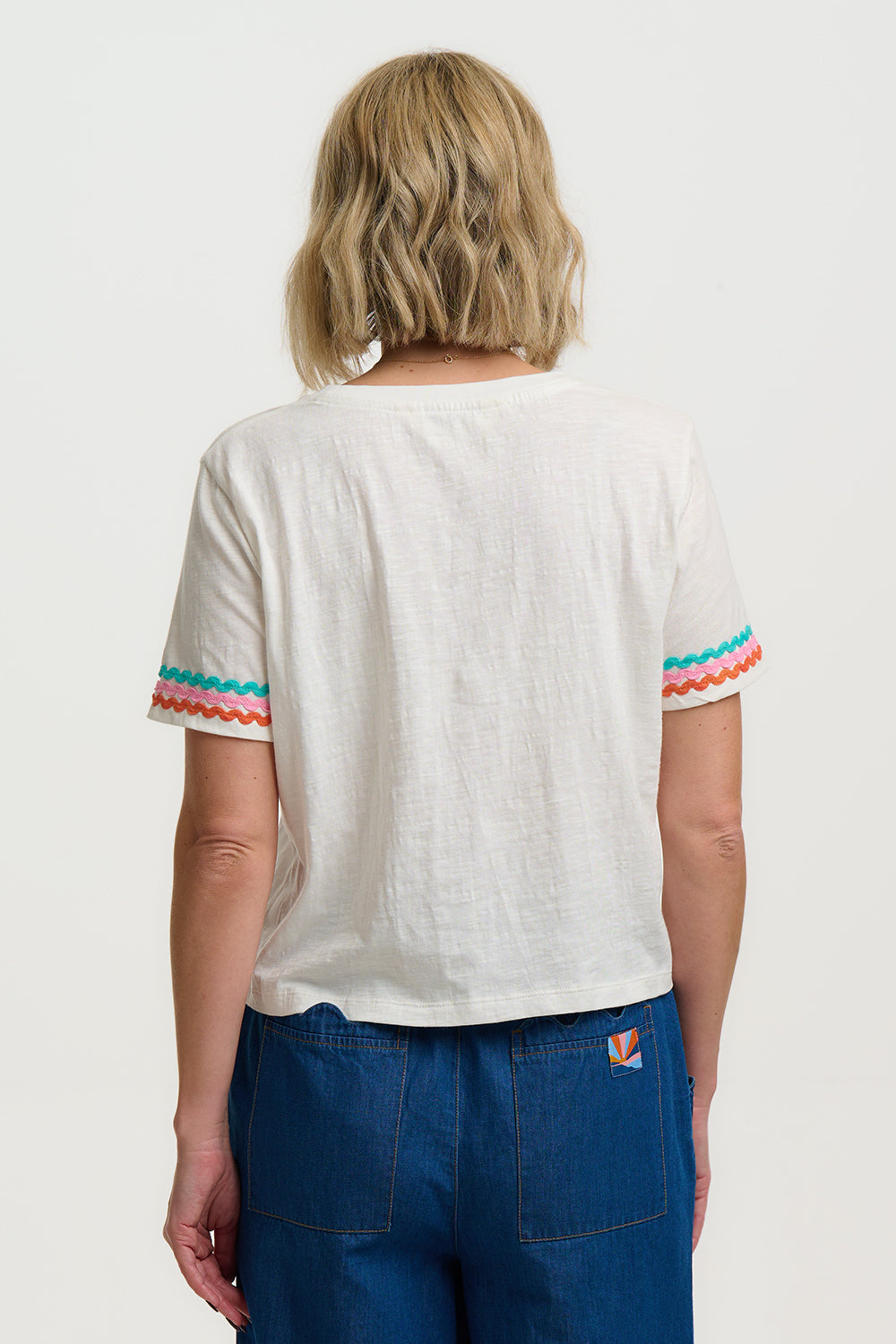 Person wearing a white t-shirt with colorful sleeves on a plain background