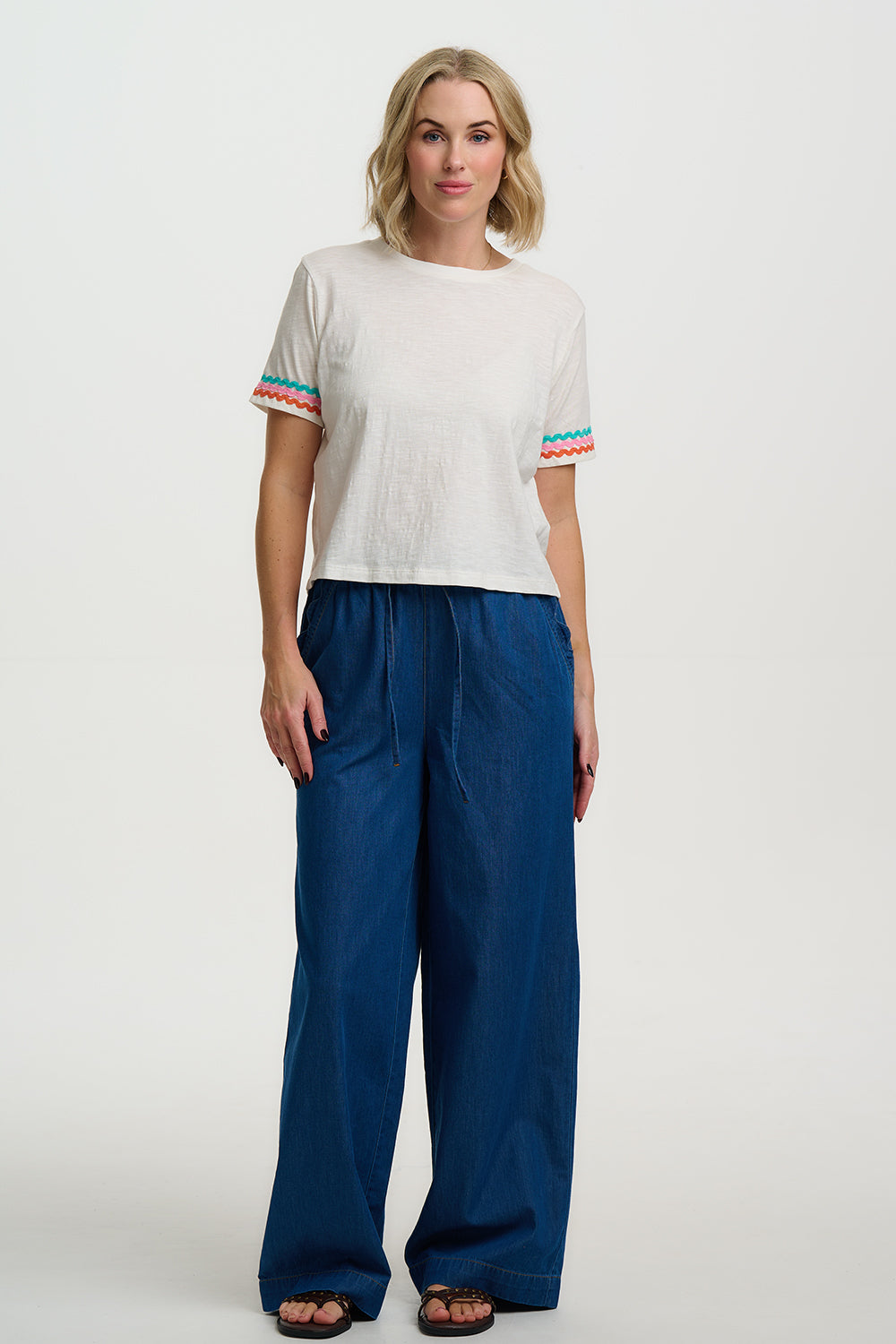 Woman wearing a white top with colorful sleeves and blue pants on a white background