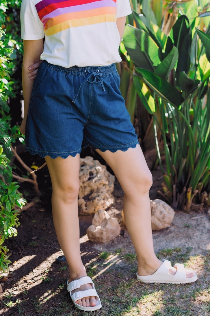 Woman wearing a colorful striped shirt and blue shorts standing in a garden.