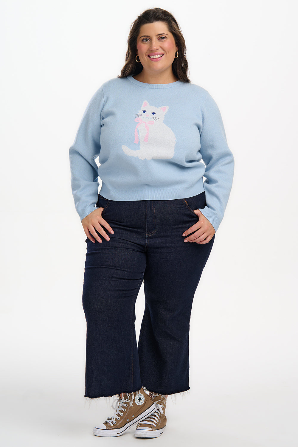 Person wearing a light blue sweater with a cat design and dark blue pants on a white background