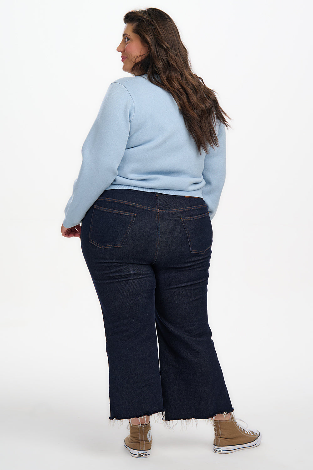 Woman wearing a light blue sweater and dark blue jeans on a white background