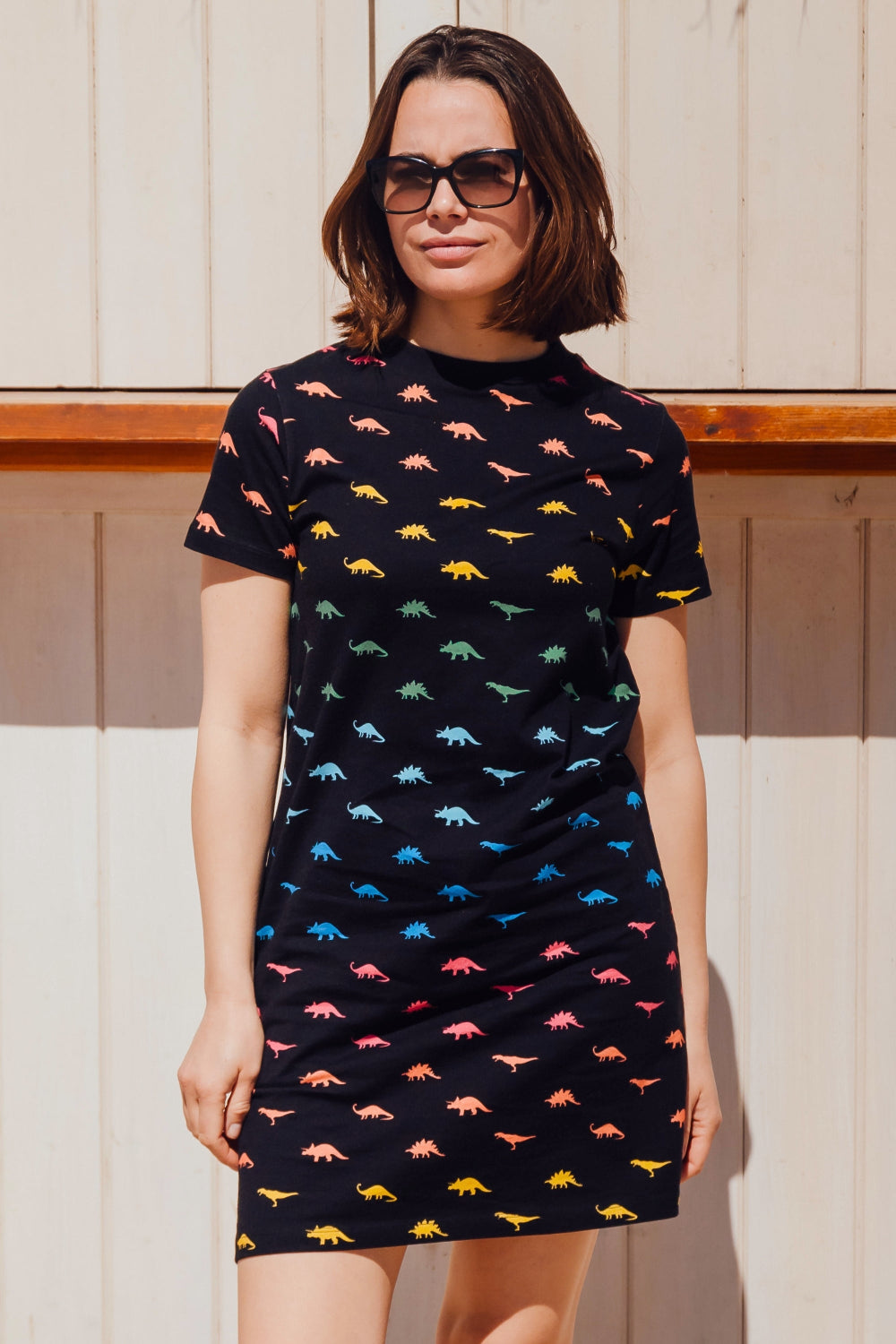 A woman wearing a black t-shirt dress with a multicolored dinosaur pattern.