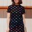 A woman wearing a black t-shirt dress with a multicolored dinosaur pattern.