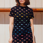 A woman wearing a black t-shirt dress with a multicolored dinosaur pattern.