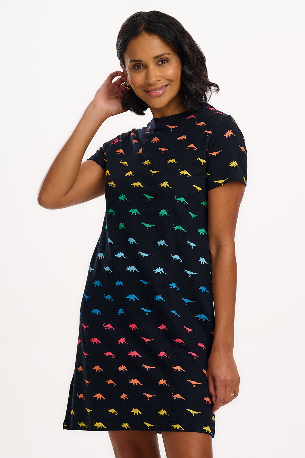 A woman smiling and posing in a black t-shirt dress with a multicolored dinosaur pattern.