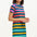 A model wearing a knee-length T-shirt dress with a colorful striped pattern in green, orange, pink, and aqua, paired with short sleeves and a round neckline.