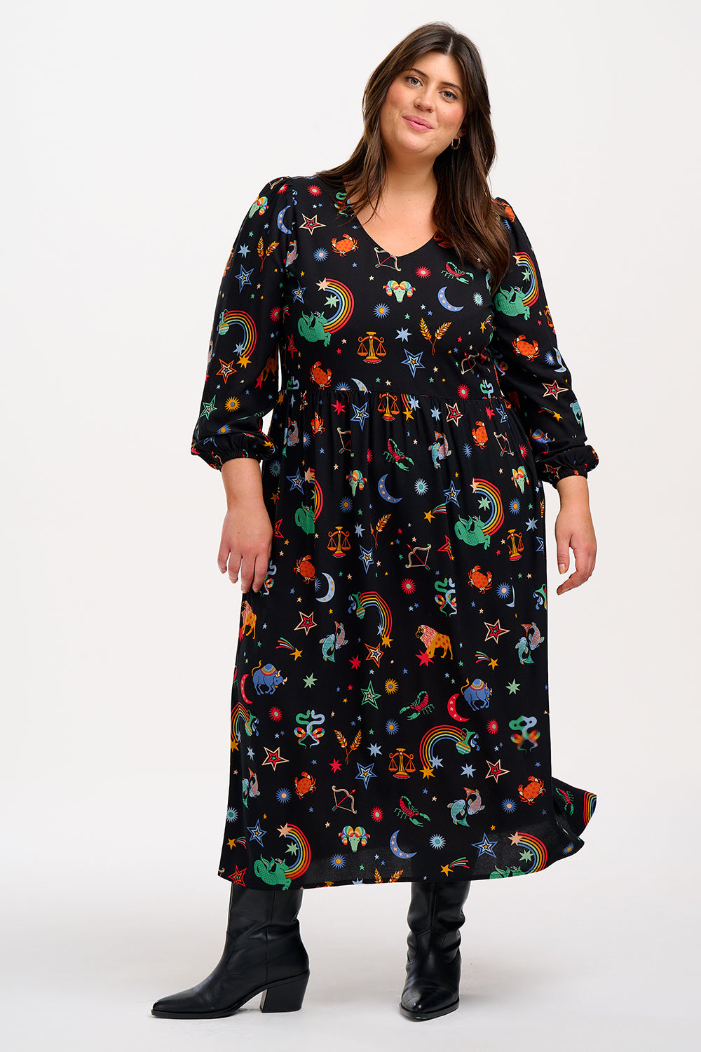 A model wearing a midi length black smock dress with a Zodiac Rainbow Skies print, featuring full blouson sleeves and a V-neck.
