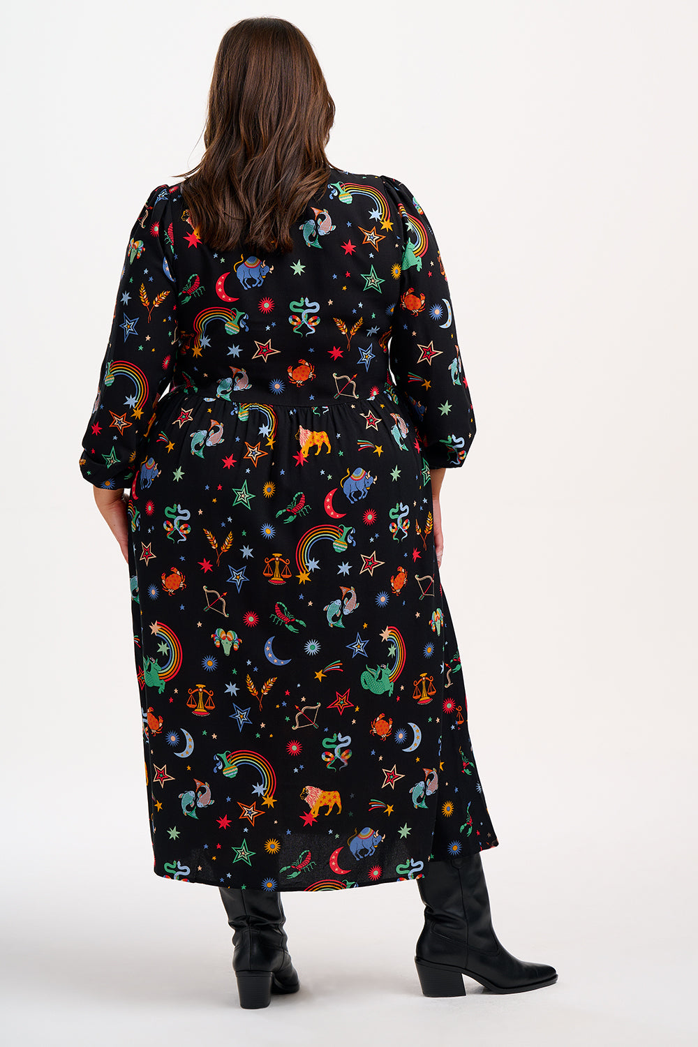 A model wearing a midi length black smock dress with a Zodiac Rainbow Skies print, featuring full blouson sleeves and a V-neck.