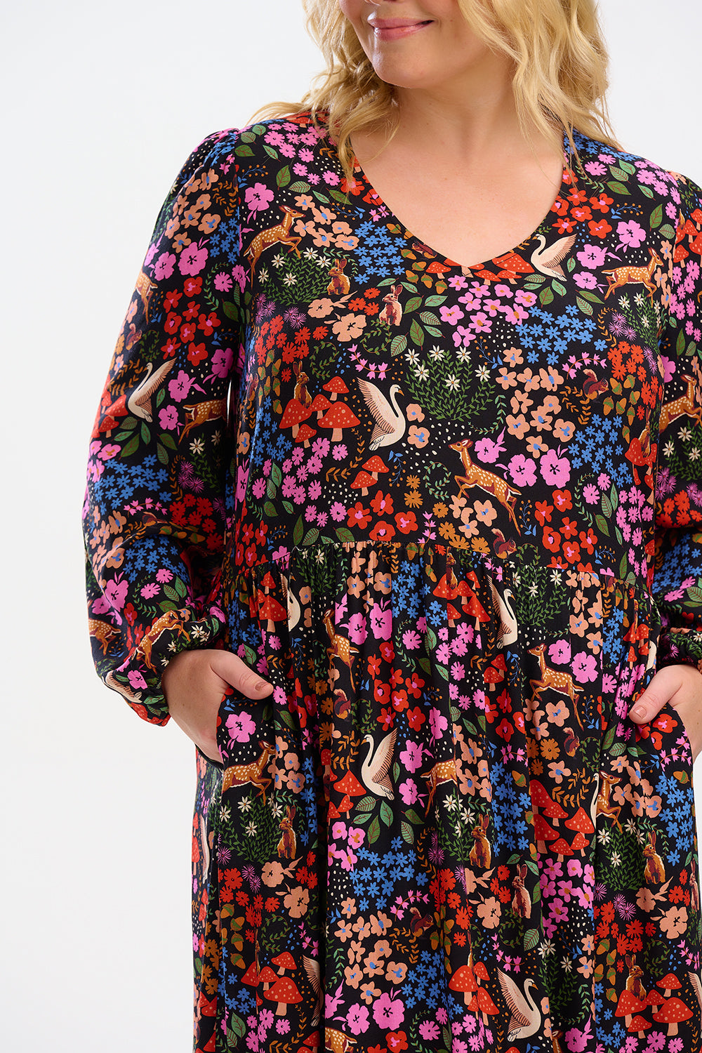 A model wearing a midi length smock dress with a vibrant woodland floral print, featuring long sleeves and a V-neck.