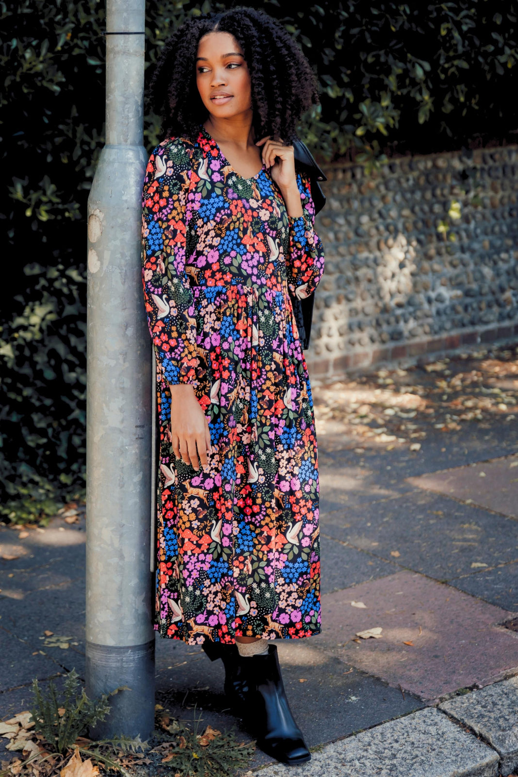 A model wearing a midi length smock dress with a vibrant woodland floral print, featuring long sleeves and a V-neck.