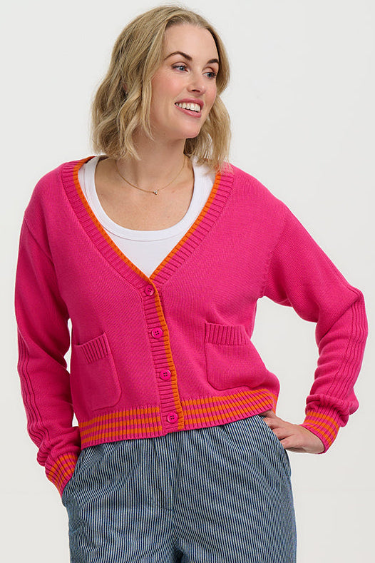 Woman wearing a bright pink cardigan with orange trim on a white background