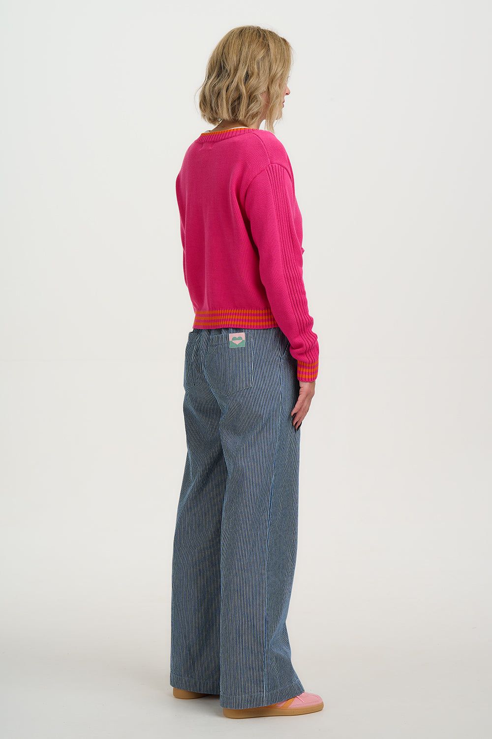 Person wearing a bright pink sweater and blue jeans on a white background
