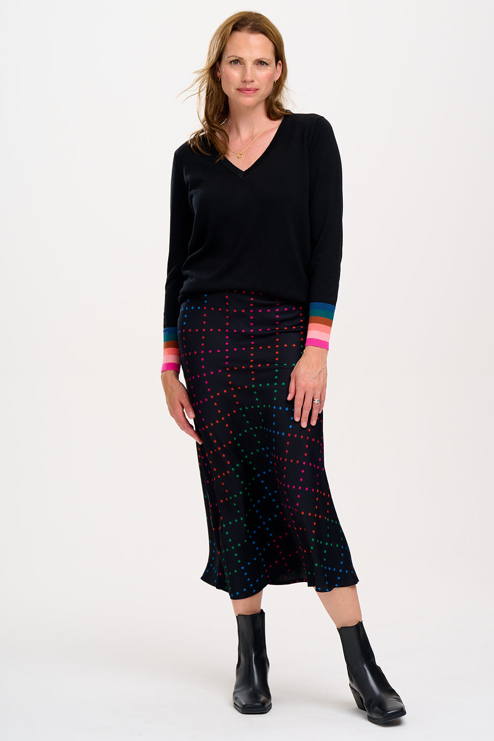 A woman wearing a midi skirt with a rainbow star lattice print in black, paired with a black top and boots. The skirt has a midi length and an elasticated waist.