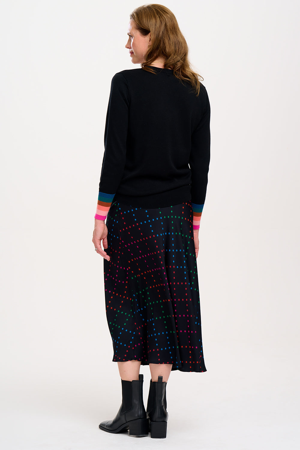 A woman wearing a midi skirt with a rainbow star lattice print in black, paired with a black top and boots. The skirt has a midi length and an elasticated waist.