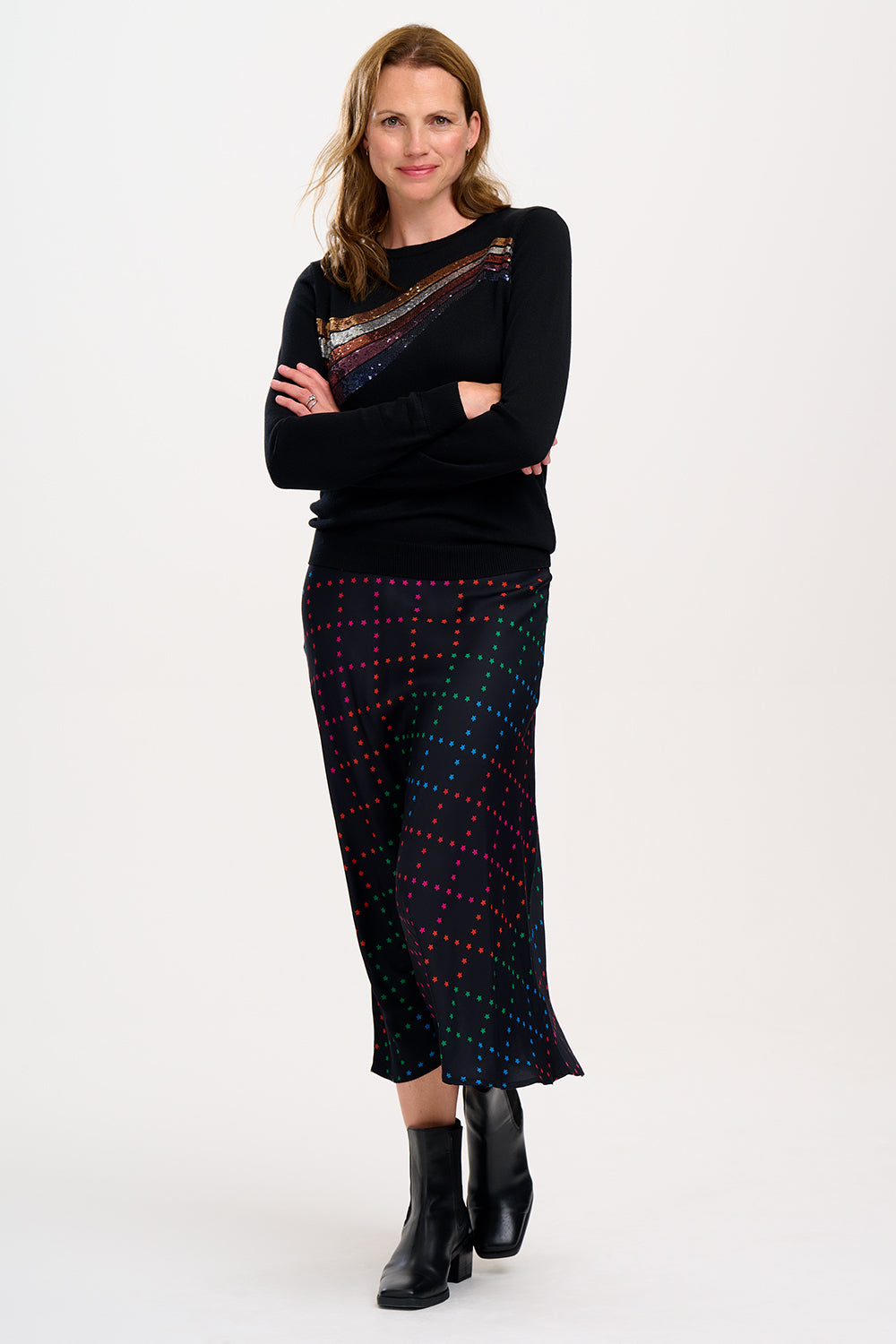 A woman wearing a midi skirt with a rainbow star lattice print in black, paired with a black top and boots. The skirt has a midi length and an elasticated waist.