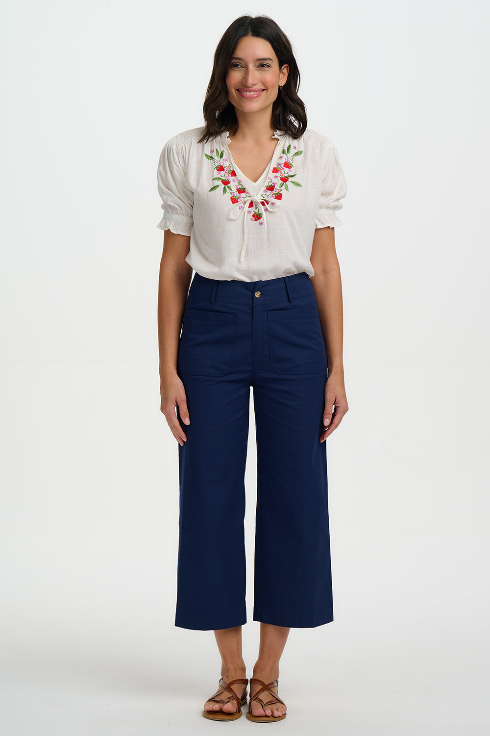 Woman wearing a white blouse with floral embroidery and blue pants on a white background