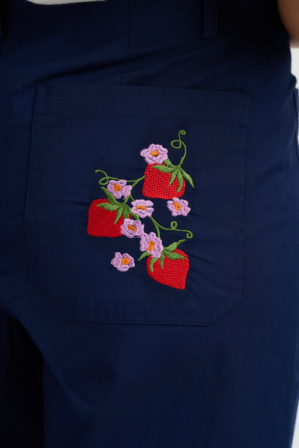 Navy blue apron with embroidered red pots and pink flowers on a white background