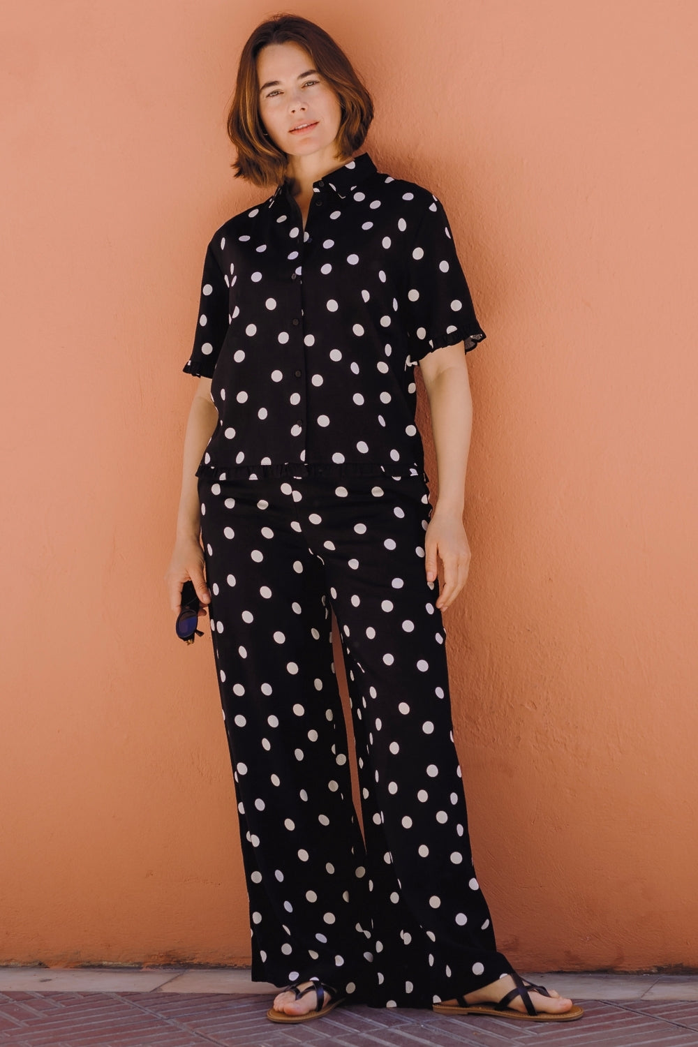 Person wearing a black polka dot jumpsuit against a brown wall