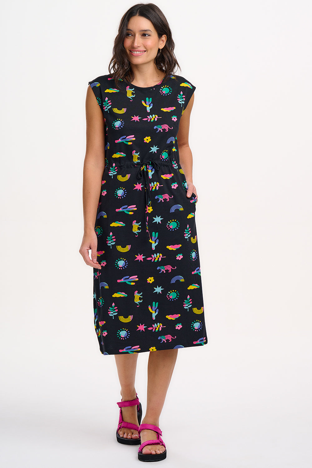 A model wearing a black midi dress with a colorful animal and floral print, standing against a white background.