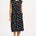 A model wearing a black midi dress with a colorful animal and floral print, standing against a white background.