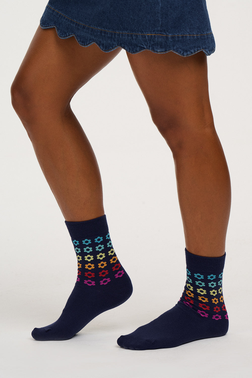 A person's legs wearing navy blue crew socks with a colorful geometric pattern near the cuffs, paired with a denim skirt against a plain light background.