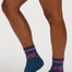 A person wearing dark blue crew socks with pink and purple striped cuffs and a pink tiger graphic, paired with a blue denim skirt against a light gray studio background.
