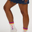 White crew socks with a rainbow stripe at the top and three colorful stars on each sock, worn by a model in a denim skirt.