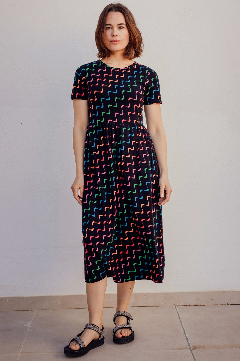 A model wearing a midi-length jersey dress with a geometric undulating waves pattern, featuring a round neck, short sleeves, and elasticated waistband.