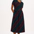 A model wearing a midi-length jersey cotton dress with a round neckline, elasticated waistband, short sleeves, and a pattern of undulating waves in black, red, and green.