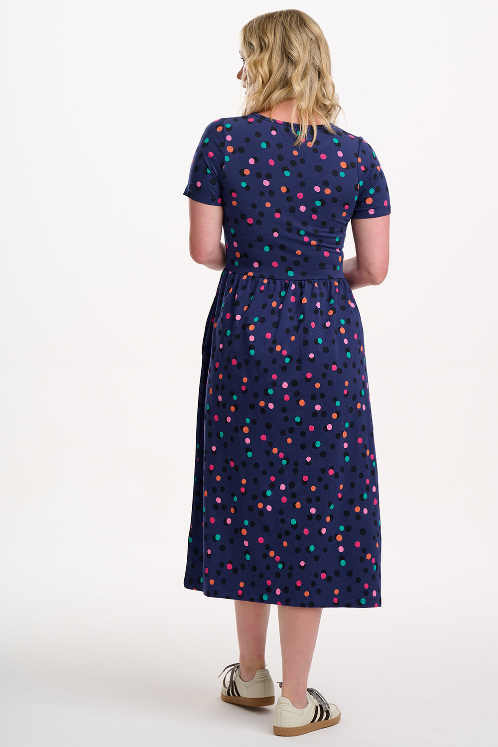 Woman wearing a navy dress with colorful polka dots on a white background