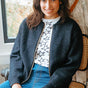Woman sitting on a chair wearing a dark gray cardigan over a star-patterned shirt and blue jeans.