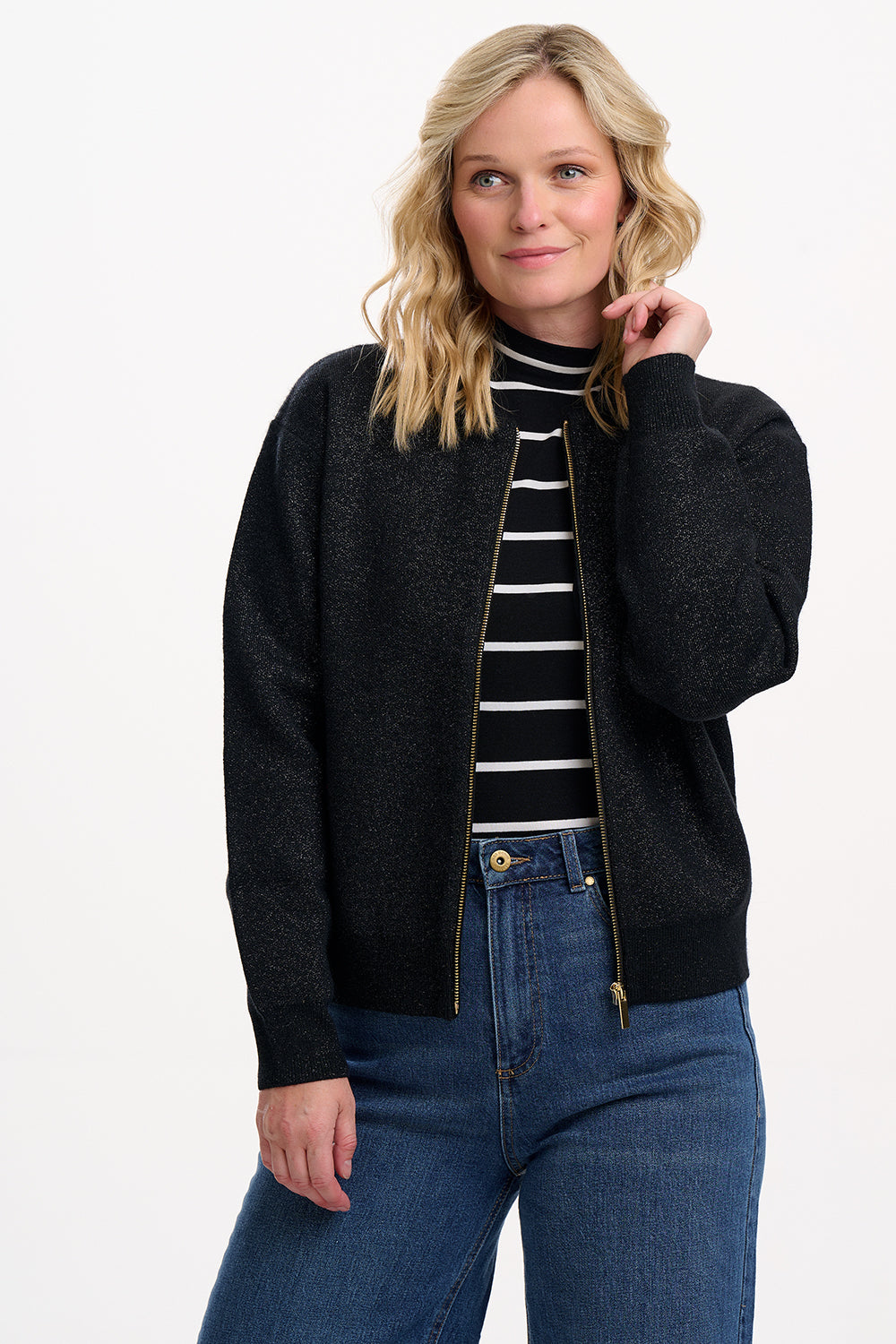 Woman wearing a black bomber jacket, black and white striped shirt, and blue jeans on a white background