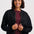 A woman wearing a dark charcoal zip-up knit jacket over a burgundy top and blue jeans, standing against a light gray studio background.