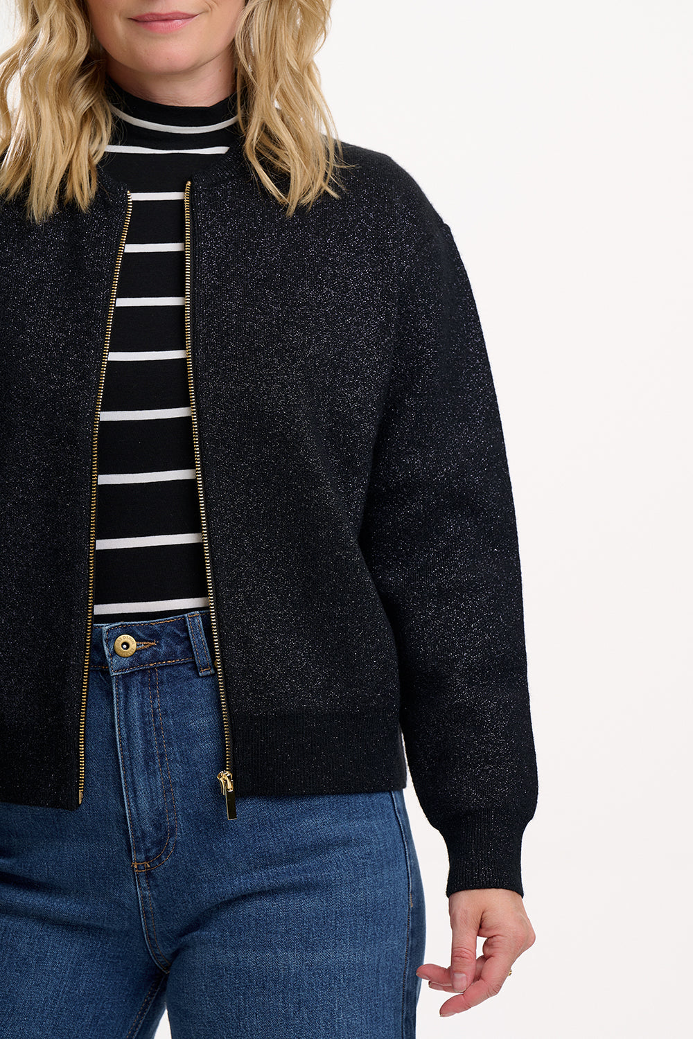 Person wearing a black bomber jacket over a striped shirt with blue jeans on a white background