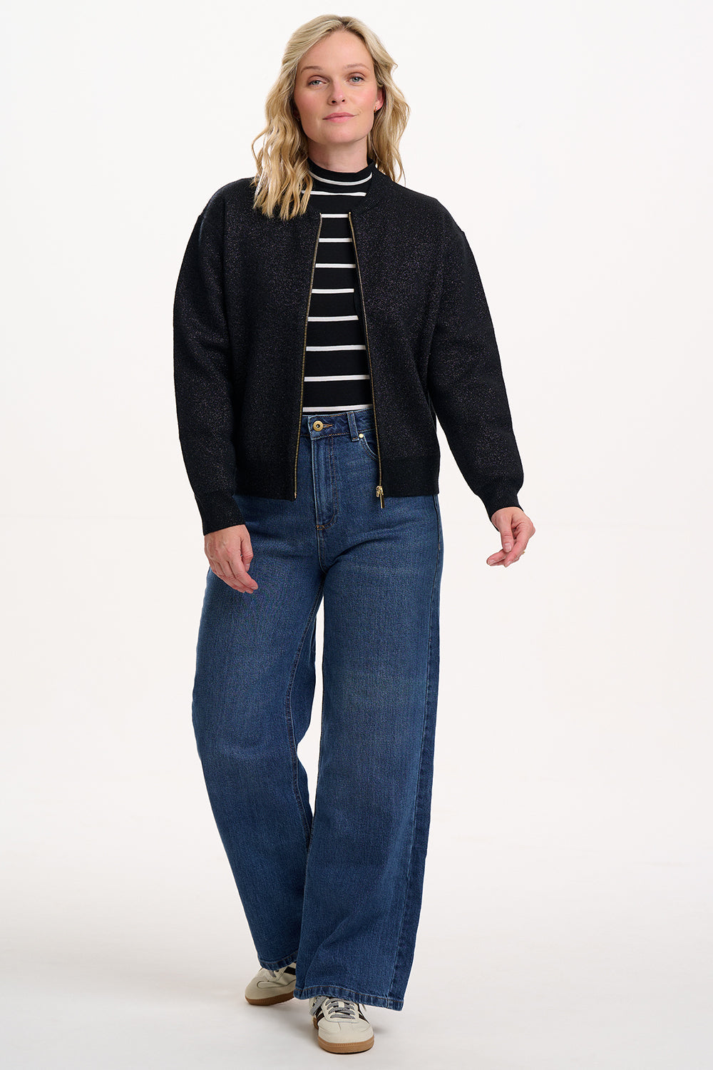 Woman wearing a black cardigan, striped shirt, and blue jeans on a white background