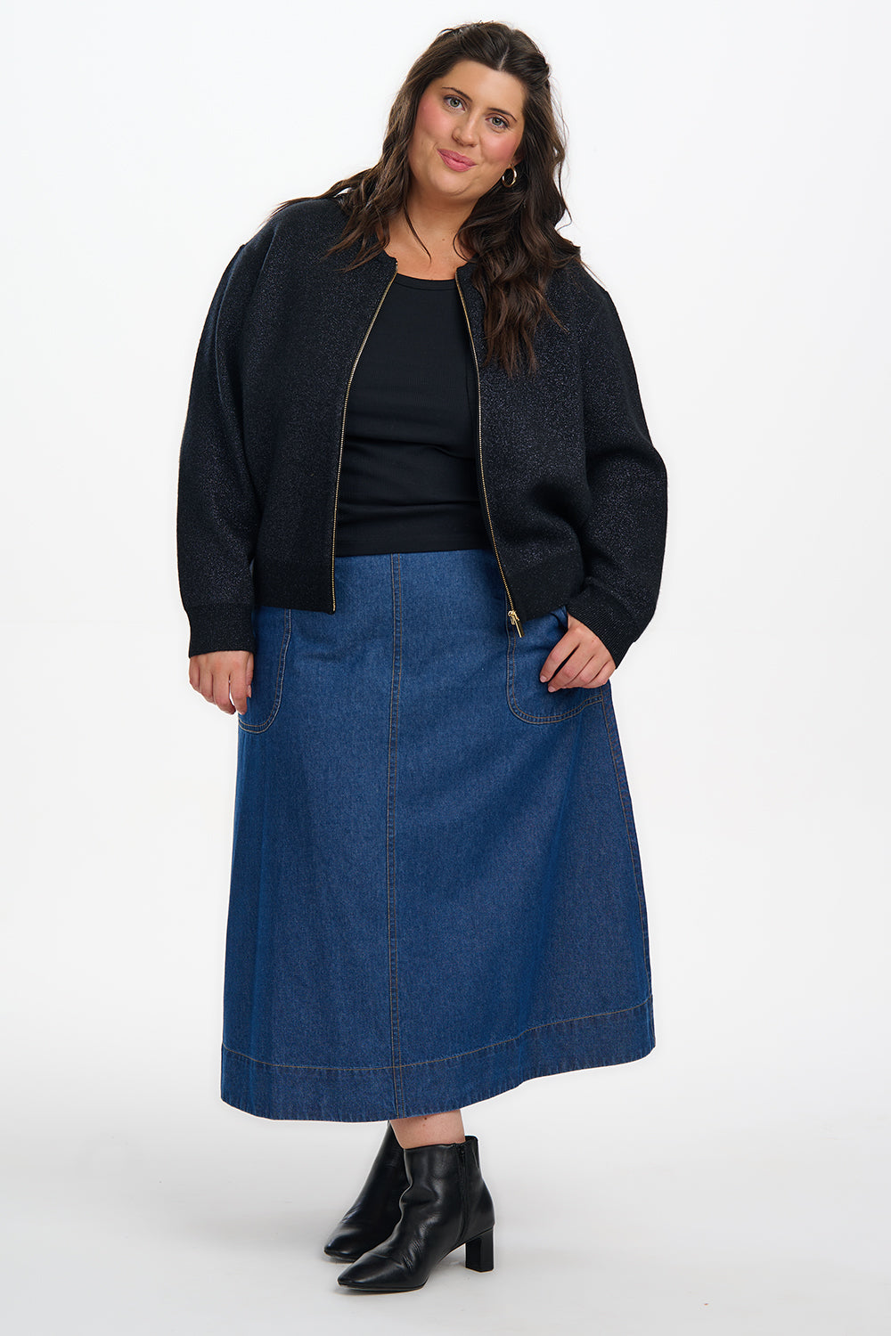 Woman wearing a black jacket, black top, and blue denim skirt on a white background