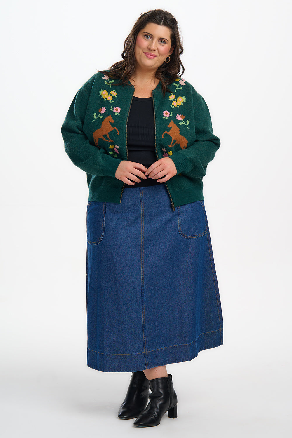 Woman wearing a green embroidered jacket and blue denim skirt on a white background